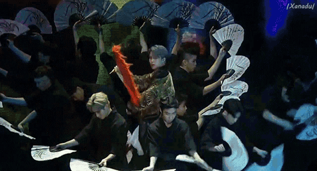 a group of people are holding fans in a dark room with the letters x and a on the bottom right