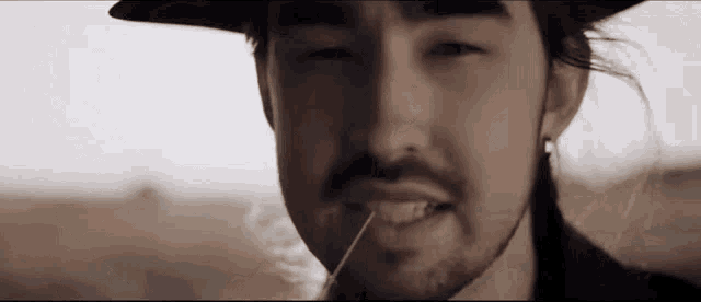 a man with long hair and a beard is smoking a cigarette in a field .