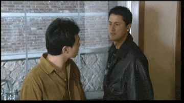 two men standing next to each other with one wearing a brown shirt and the other wearing a black jacket