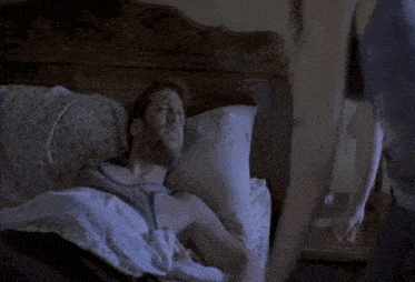 a man laying in a bed with a woman standing behind him