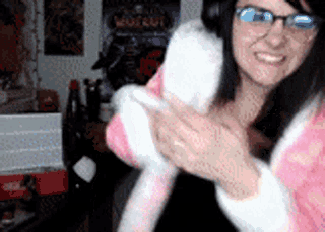 a woman wearing glasses and a pink robe holds a stuffed animal in her hands