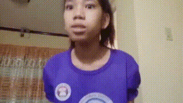 a young girl wearing a purple shirt with a rainbow on it is standing in a room .