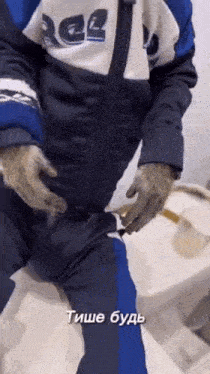 a man in a blue and white jacket is sitting on a toilet with gloves on .