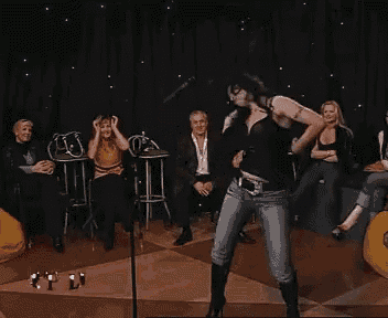 a woman in a black tank top is dancing in front of a crowd of people