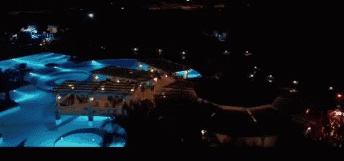 a swimming pool is lit up at night with a few people standing around it