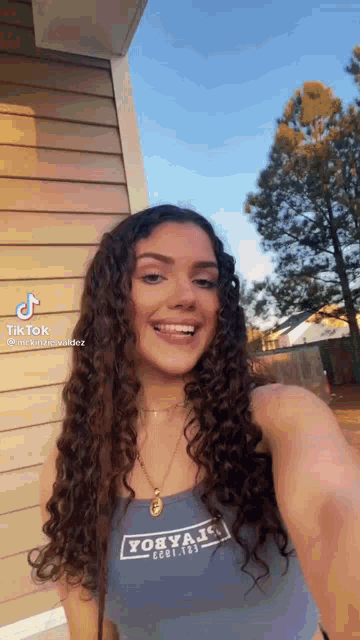 a young woman with curly hair is taking a selfie in front of a building .