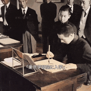 a black and white photo of a man sitting at a desk with chinese writing on it