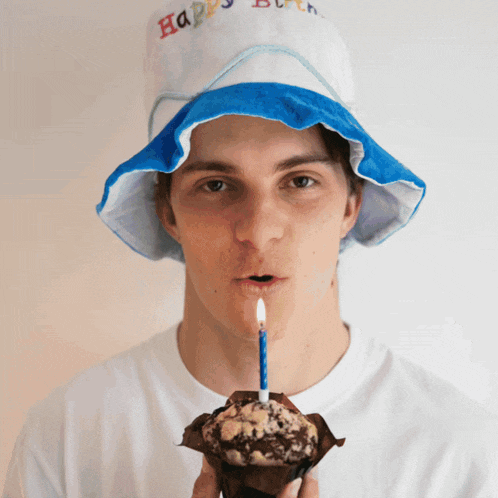 a man wearing a hat that says happy birthday is blowing out a candle on a muffin