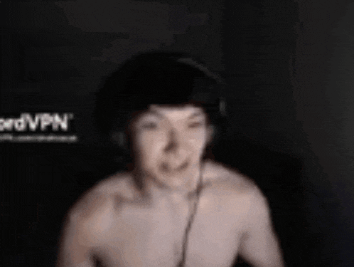 a man without a shirt is wearing headphones and smiling in a dark room .