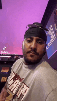 a man wearing a bandana and sunglasses is standing in front of a purple wall .