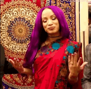 a woman with purple hair is wearing a red saree and standing in front of a rug .