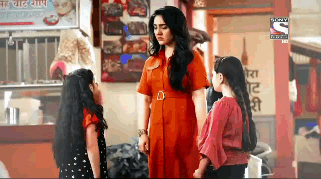 a woman in an orange dress is standing next to two girls in a restaurant .