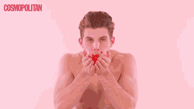 a shirtless man is blowing confetti in front of a pink background with the word cosmopolitan on it