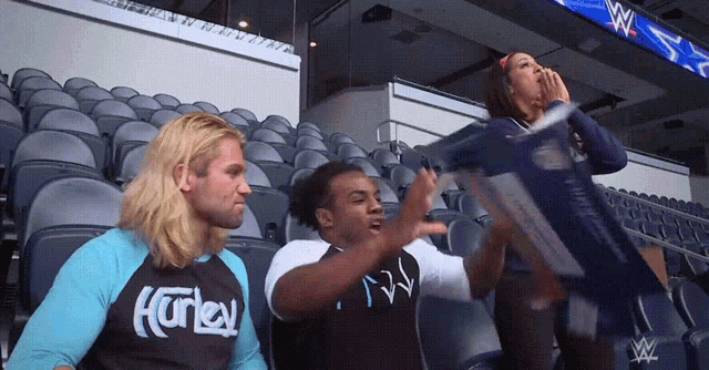 a man wearing a shirt that says hurley is sitting in a stadium with other people