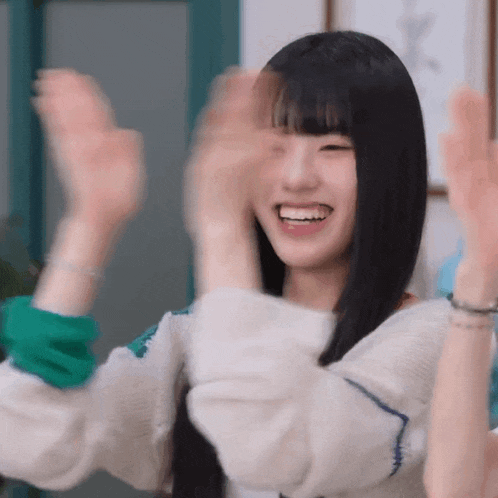 a young woman with long black hair is smiling and clapping her hands in the air .