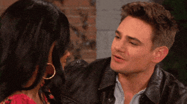 a man and a woman are looking at each other and the man is wearing a brown leather jacket