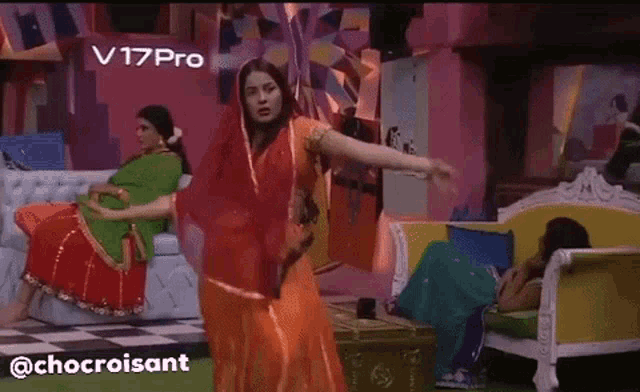a woman in an orange dress is dancing in front of a v17 pro sign