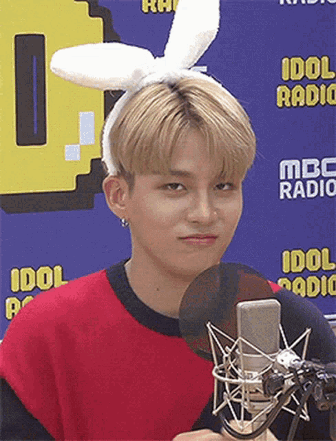 a young man wearing bunny ears stands in front of a microphone in front of a sign that says idol radio