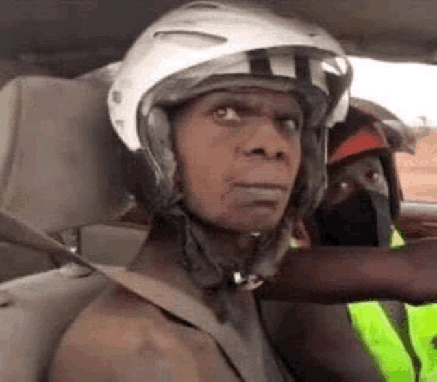 a man wearing a helmet is sitting in a car and making a funny face .