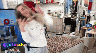 a woman in a white shirt is dancing in front of a tv screen that says los