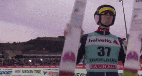 a ski jumper wearing a helvetia jersey is holding up his skis