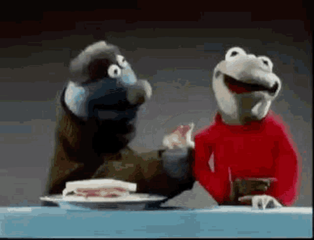 two muppets are sitting at a table with a plate of food and a sandwich .