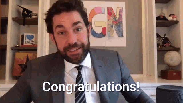 a man in a suit and tie is saying congratulations in front of a sign that says gn