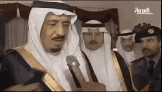a man in a white robe is talking into a microphone while standing next to a group of men .