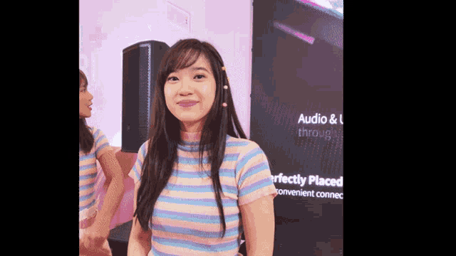 a woman in a striped shirt stands in front of a sign that says audio