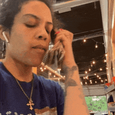 a woman wearing a blue shirt with a cross on it is talking on a cell phone