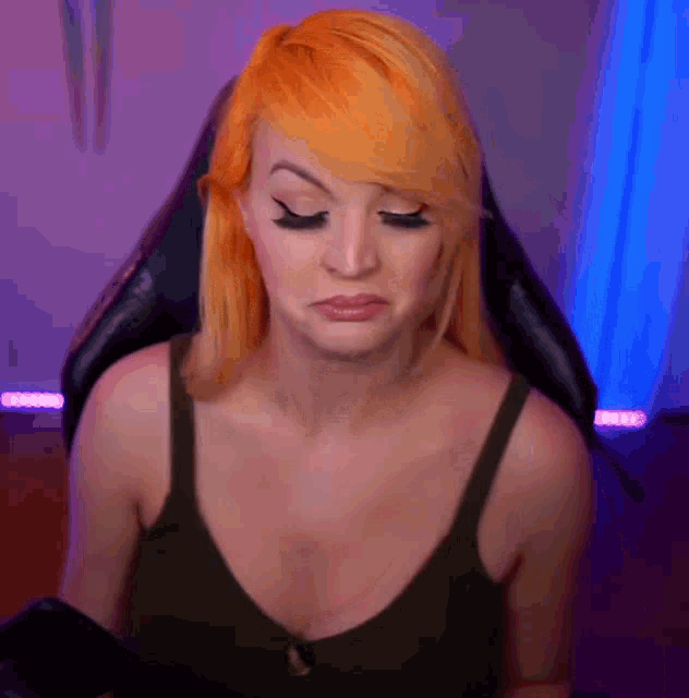 a woman with orange hair is sitting in a chair with her eyes closed and making a sad face .