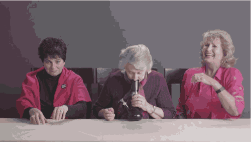 three older women are sitting at a table and one of them is smoking a bong