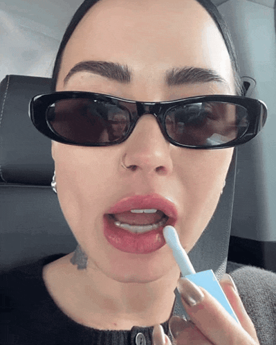 a woman wearing sunglasses is applying lipstick on her lips