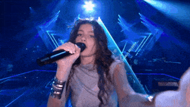a woman is singing into a microphone with a blue background