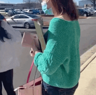 a woman in a green sweater is wearing a mask and holding a clipboard .