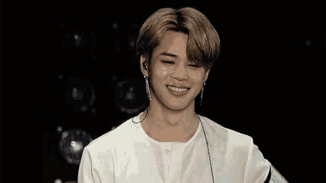 a young man wearing a white shirt and earphones smiles for the camera