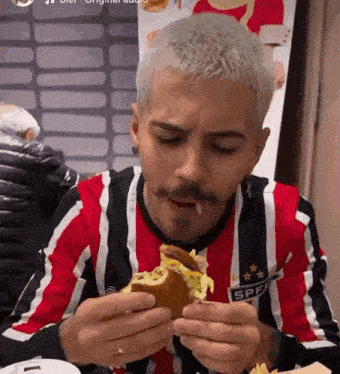 a man with a mustache is eating a hamburger while wearing a striped shirt .
