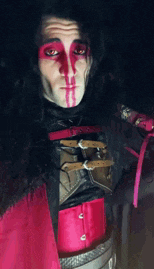a man with red paint on his face is wearing a red and black outfit