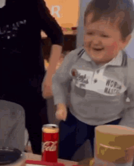 a little boy is sitting at a table with a can of coca cola .