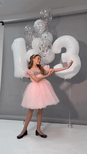 a girl in a pink dress holds a number 3 balloon in her hand