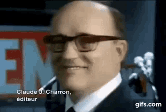 a bald man wearing glasses and a suit is smiling in front of a microphone .