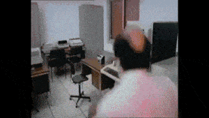a bald man is standing in a room with a desk and chair