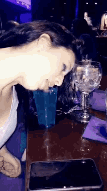 a woman is drinking a blue drink from a glass