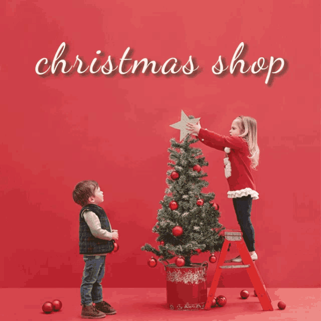 a boy and a girl decorating a christmas tree with the words christmas shop behind them
