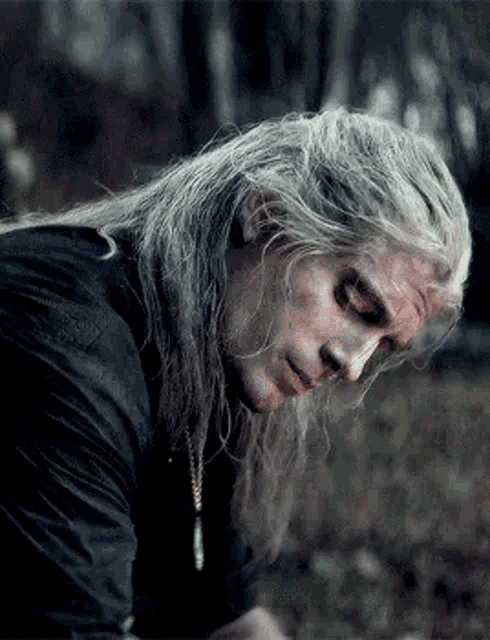 a man with long gray hair is laying down in the woods .