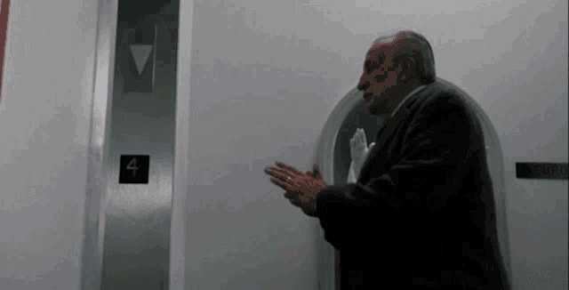 a man in a suit is standing in front of an elevator with the number four on it