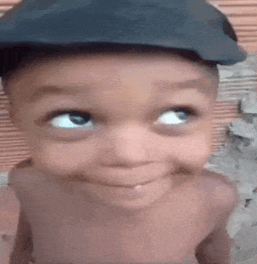 a shirtless child wearing a hat is smiling and looking up .