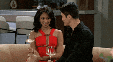 a woman in a red dress is holding a glass of wine next to a man in a black shirt