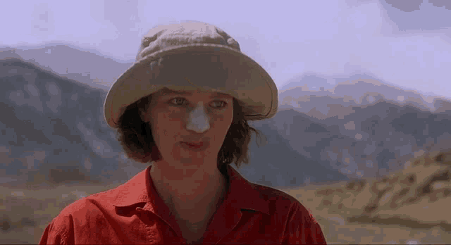 a woman wearing a hat and a red shirt has a patch on her nose