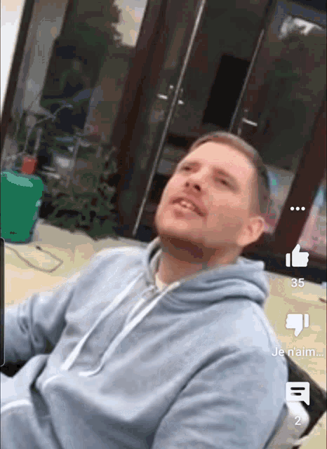 a man in a blue hoodie is sitting in front of a green propane tank and a window